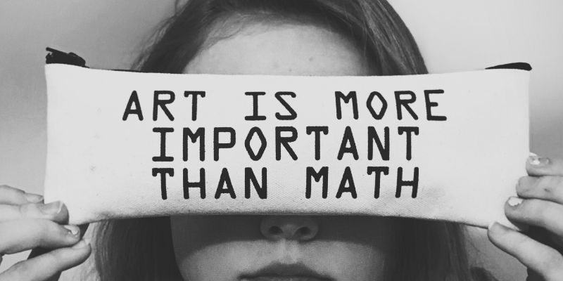 Woman holding a cushion in front of her eyes that says Maths is more important than art